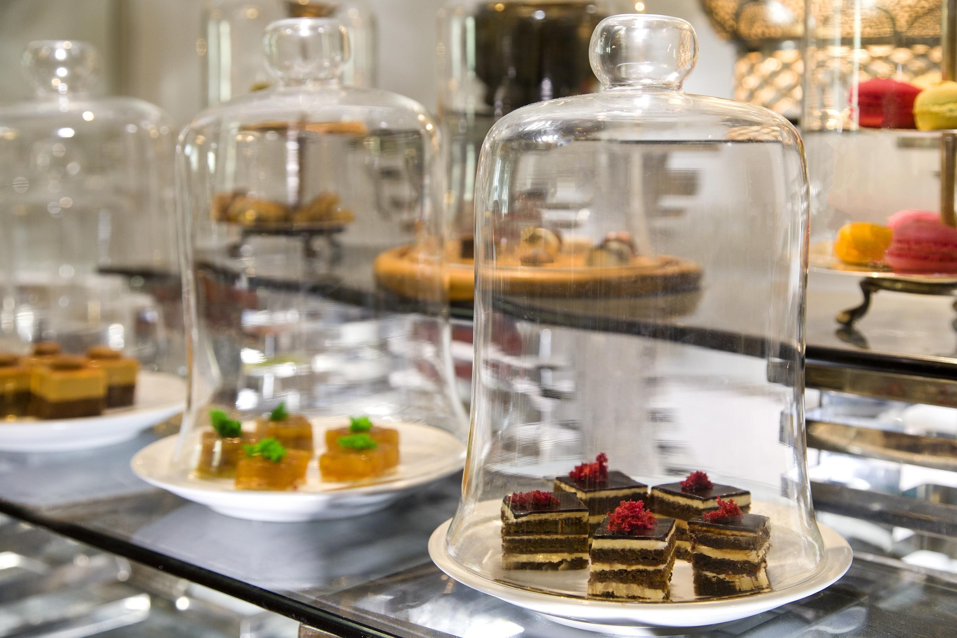 Una presentación de postres con varios pasteles bajo campanas de cristal.