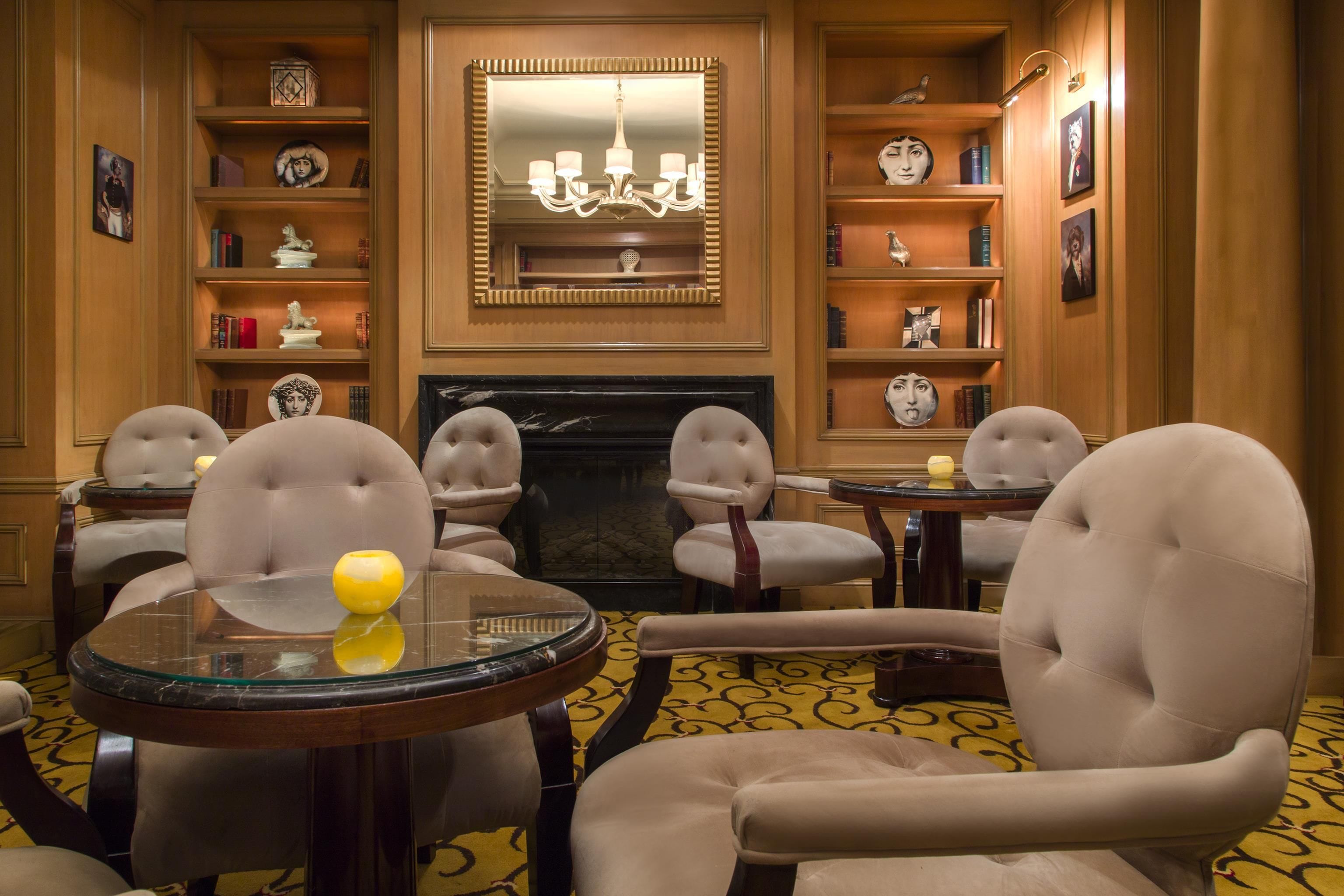 A room with a fireplace, bookshelves, a chandelier, and four upholstered chairs.