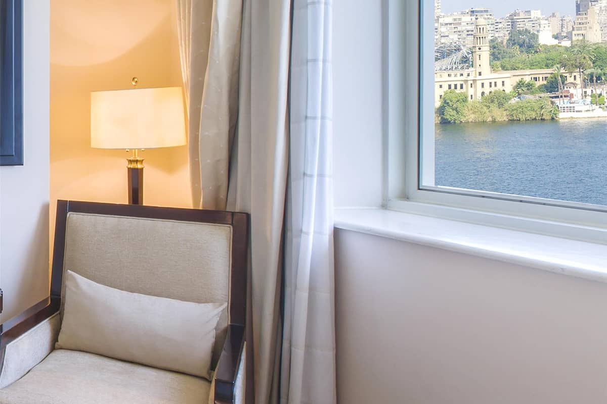 Una camera d'hotel con un letto, una sedia, una lampada, una finestra con vista sulla città e tende.