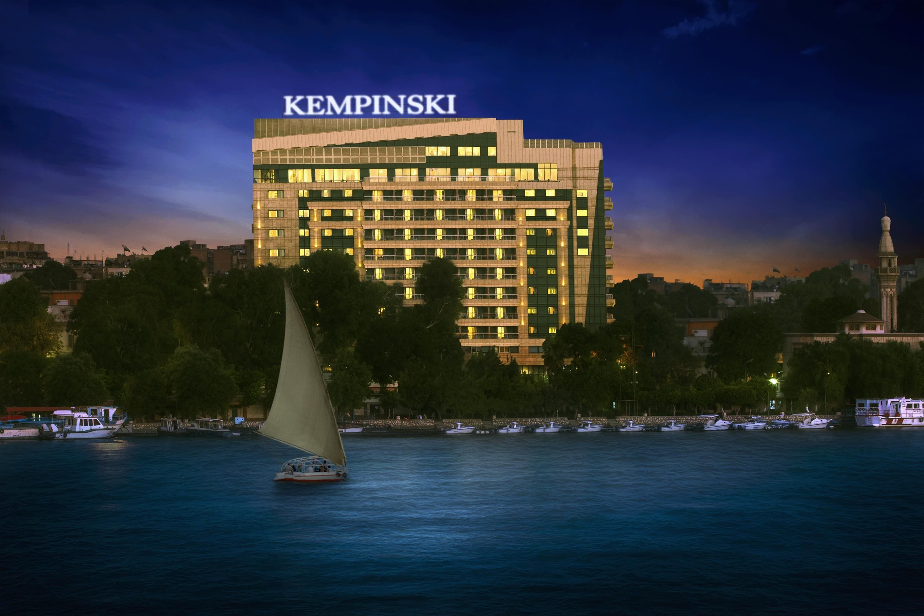 A large hotel building with the name 'KEMPINSKI' at the top, situated by a body of water with several boats.