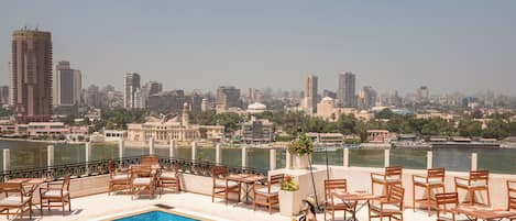 Una piscina en la azotea con vistas a la ciudad, rodeada de sillones y mesas.
