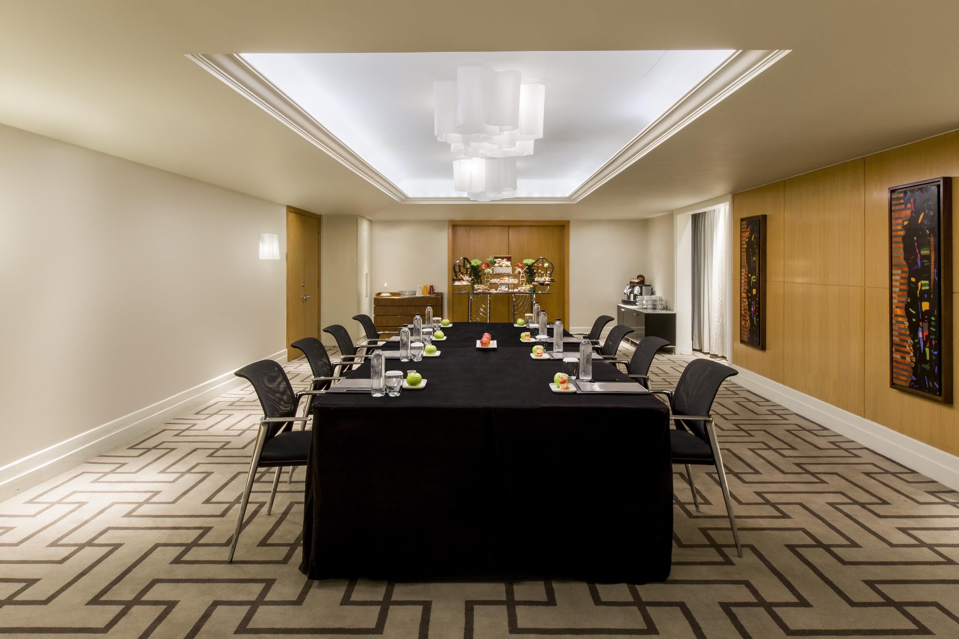 Une salle de conférence avec une longue table, des chaises, un lustre et un élément décoratif mural.