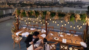 A rooftop dining area with a city view, tables set for a meal, and a couple dancing. - Kempinski Nile Hotel Cairo (Cairo)