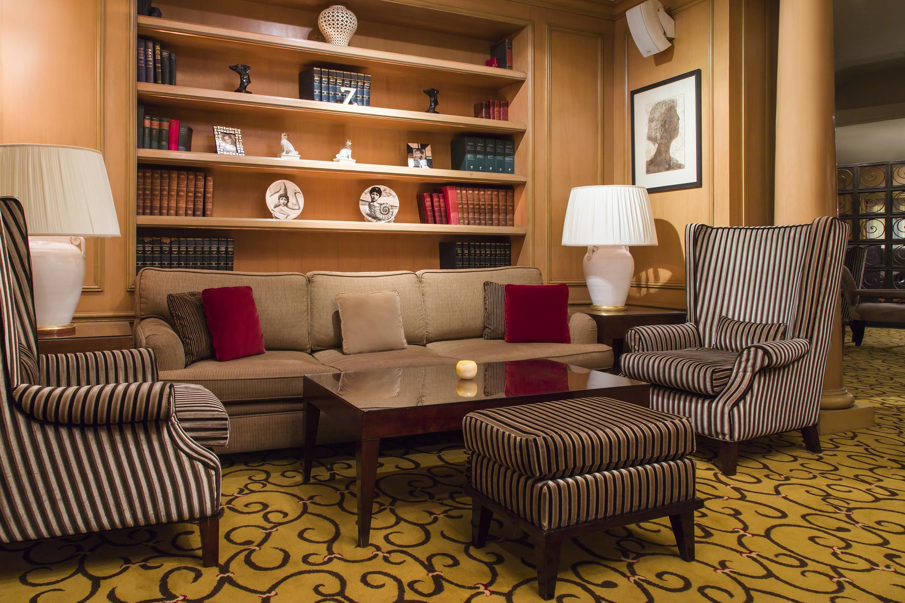 A cozy seating area with a sofa and striped armchairs, a coffee table, and a bookshelf filled with books and decorative items.