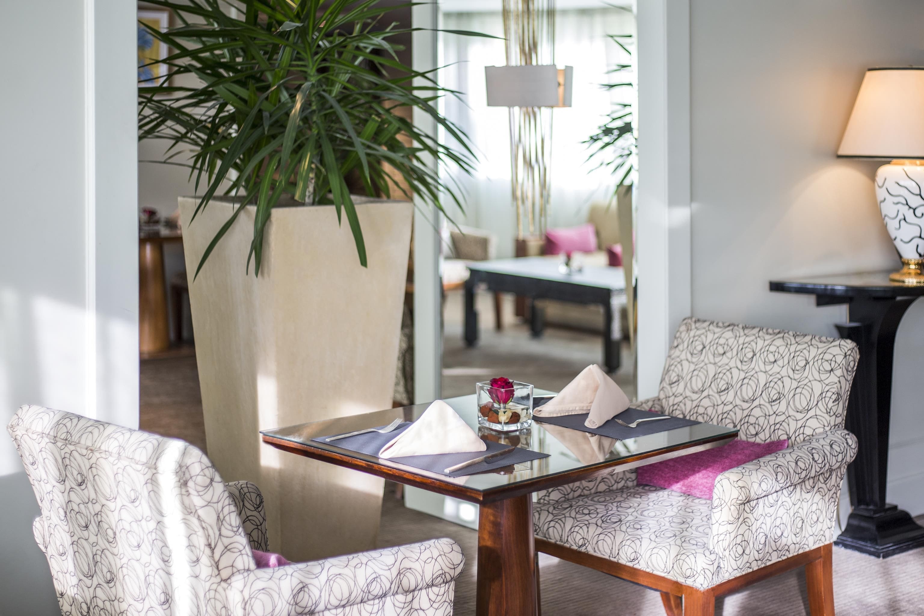 Un comedor moderno con una mesa de vidrio, sillas estampadas, una planta en maceta y una lámpara.