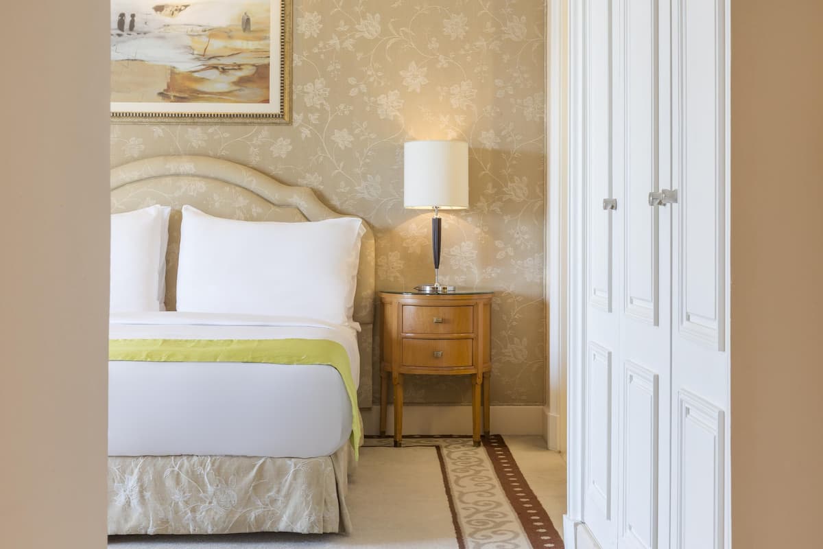 Una camera d'albergo ordinata con un letto, un comodino, una lampada e un armadio.