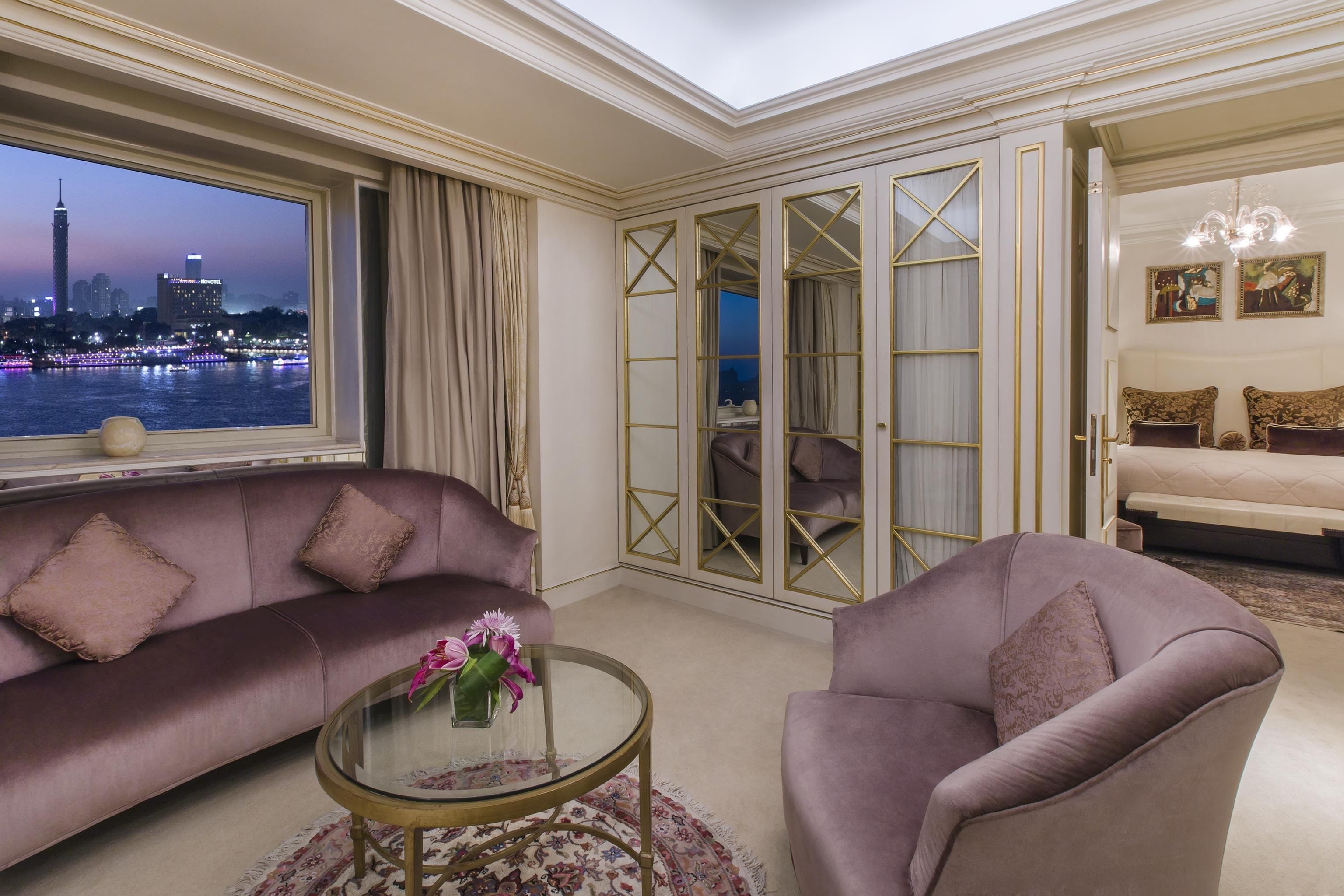 Uma sala de estar moderna com vista para a cidade, um sofá, poltrona e uma mesa de centro de vidro.