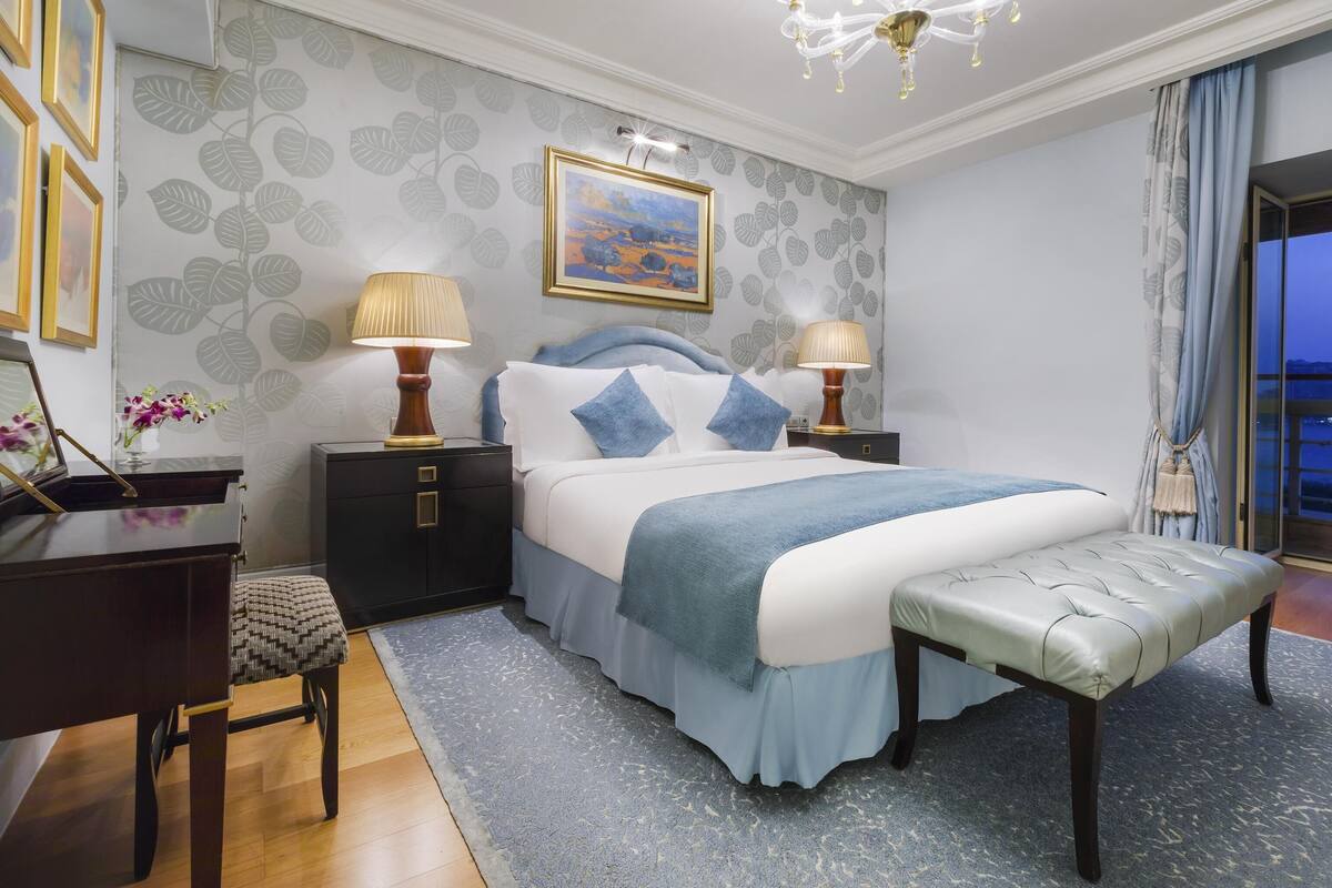 Camera d'albergo con un letto, due comodini con lampade, una scrivania, una sedia e vista sull'esterno.