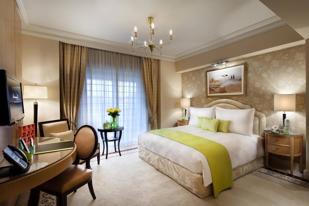 Camera d'albergo con un letto grande, una scrivania con il telefono, una sedia, un tavolino con un vaso di fiori e un quadro appeso al muro.