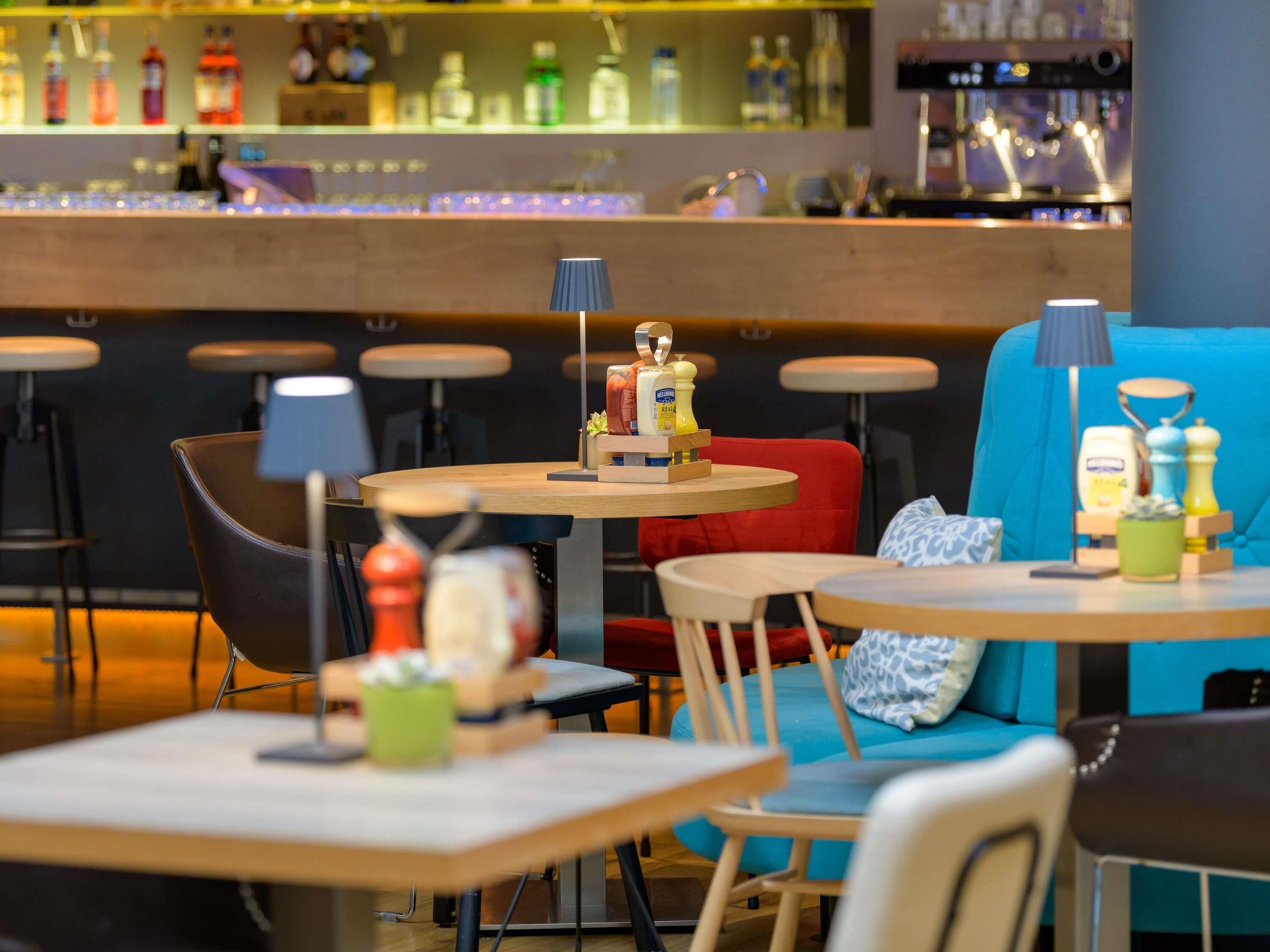 A modern bar area with a counter displaying various bottles and a seating area with tables and chairs.