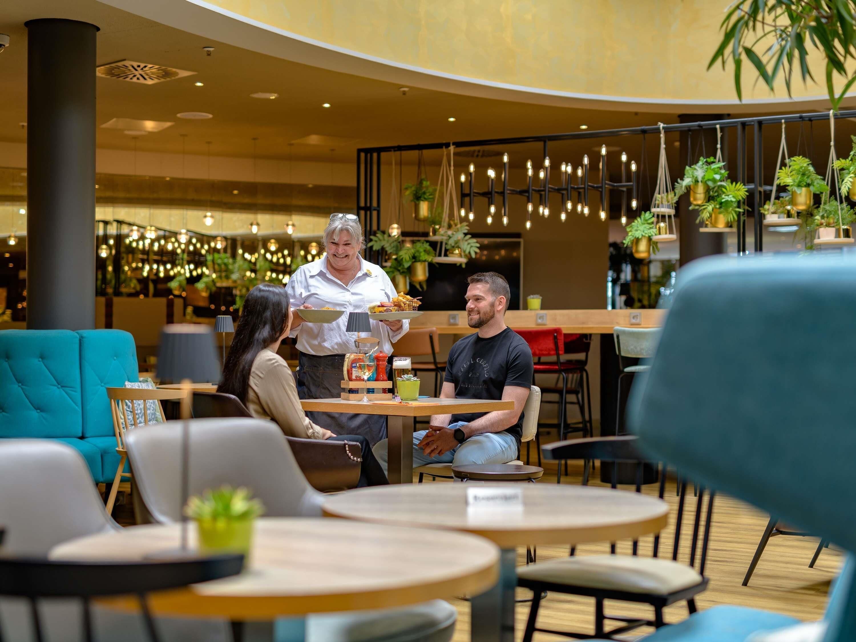 Um café moderno com mesas redondas, sofás verde-água e plantas penduradas.