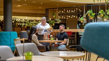 Um café moderno com mesas redondas, sofás verde-água e plantas penduradas.