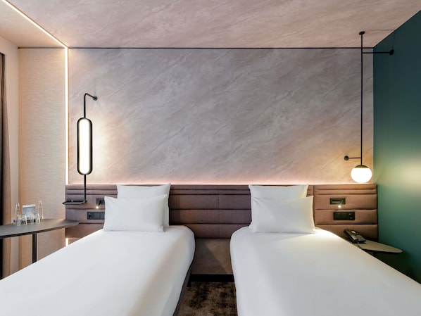 A modern hotel room with two beds, a bedside table, a nightstand, and a wall-mounted phone. - Novotel München Airport (Freising)