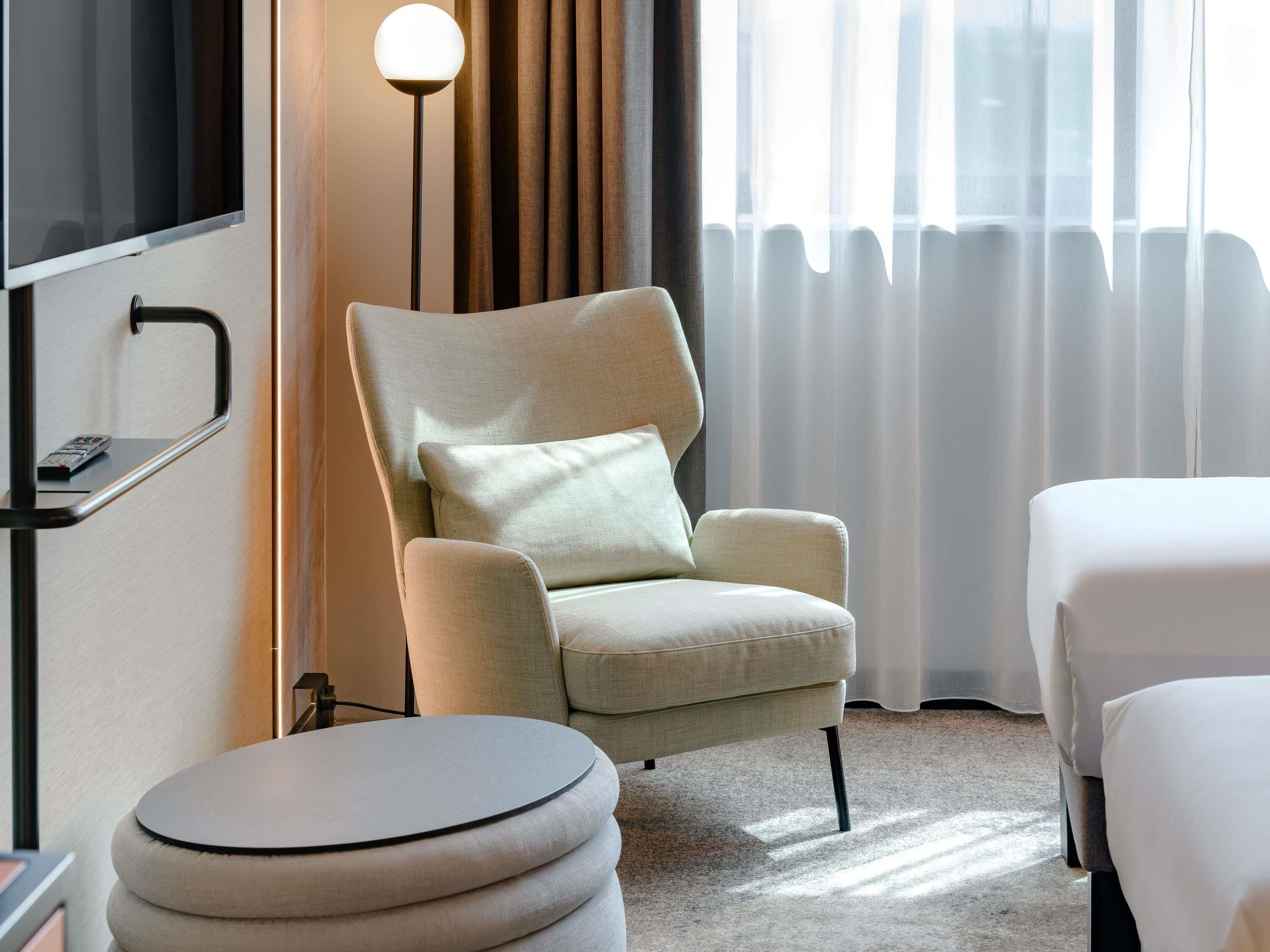 A hotel room with a sofa, ottoman, and a bed.