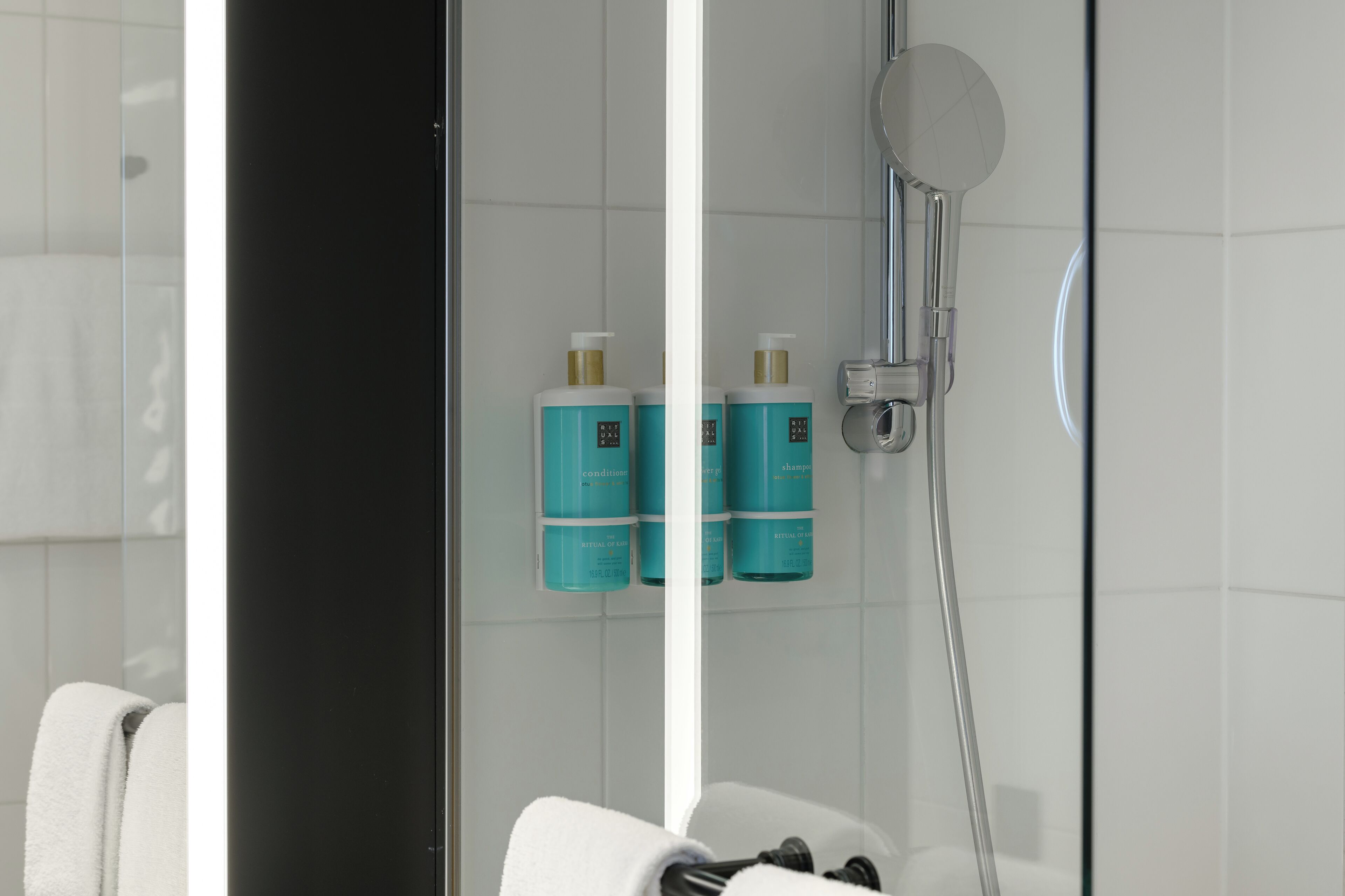 Ein modernes Badezimmer mit Duschkabine aus Glas, weißen Fliesen und zwei Shampooflaschen an der Wand.