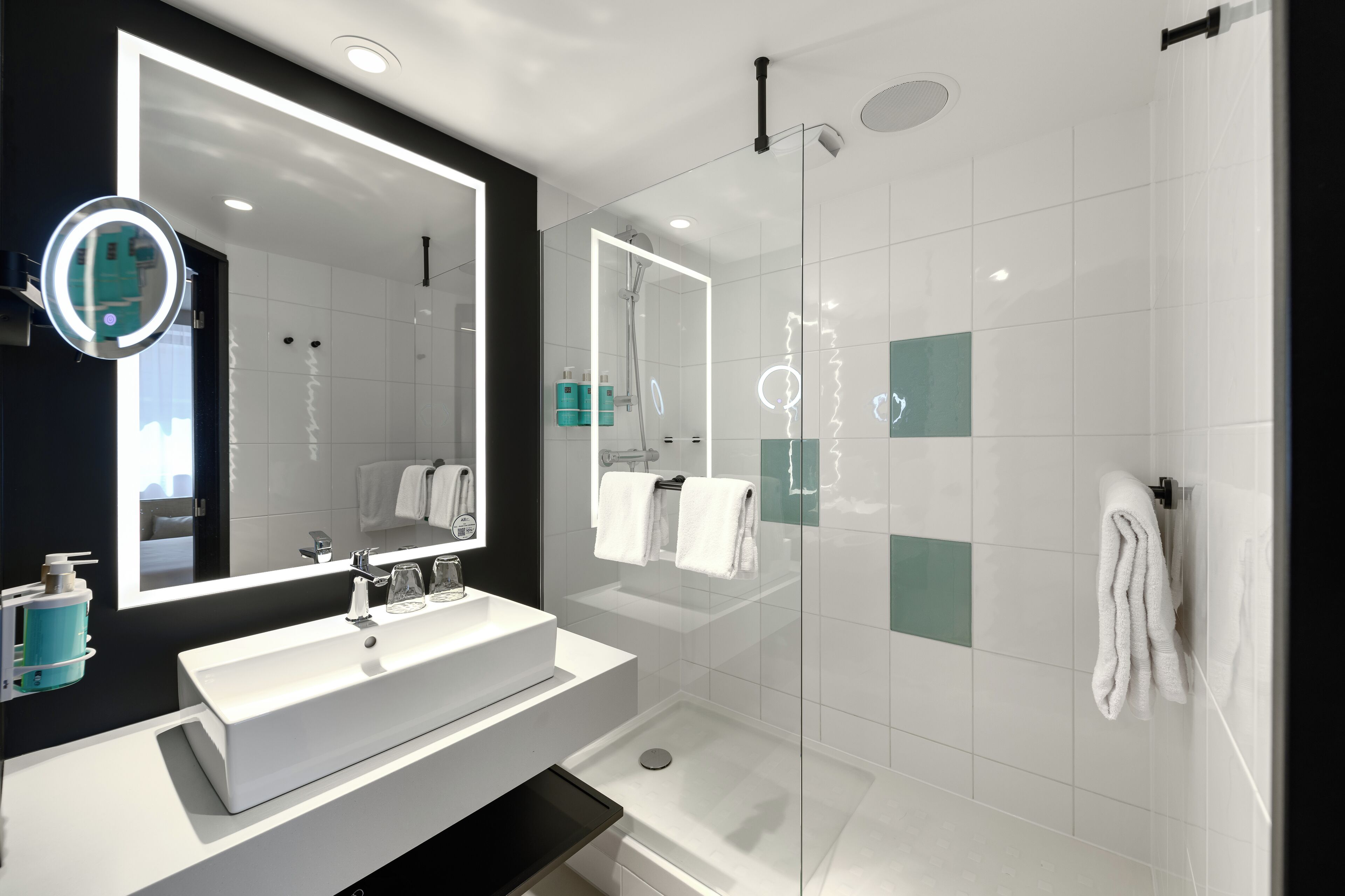 A modern bathroom with a large mirror, a white sink, a glass-enclosed shower, and a towel rack.