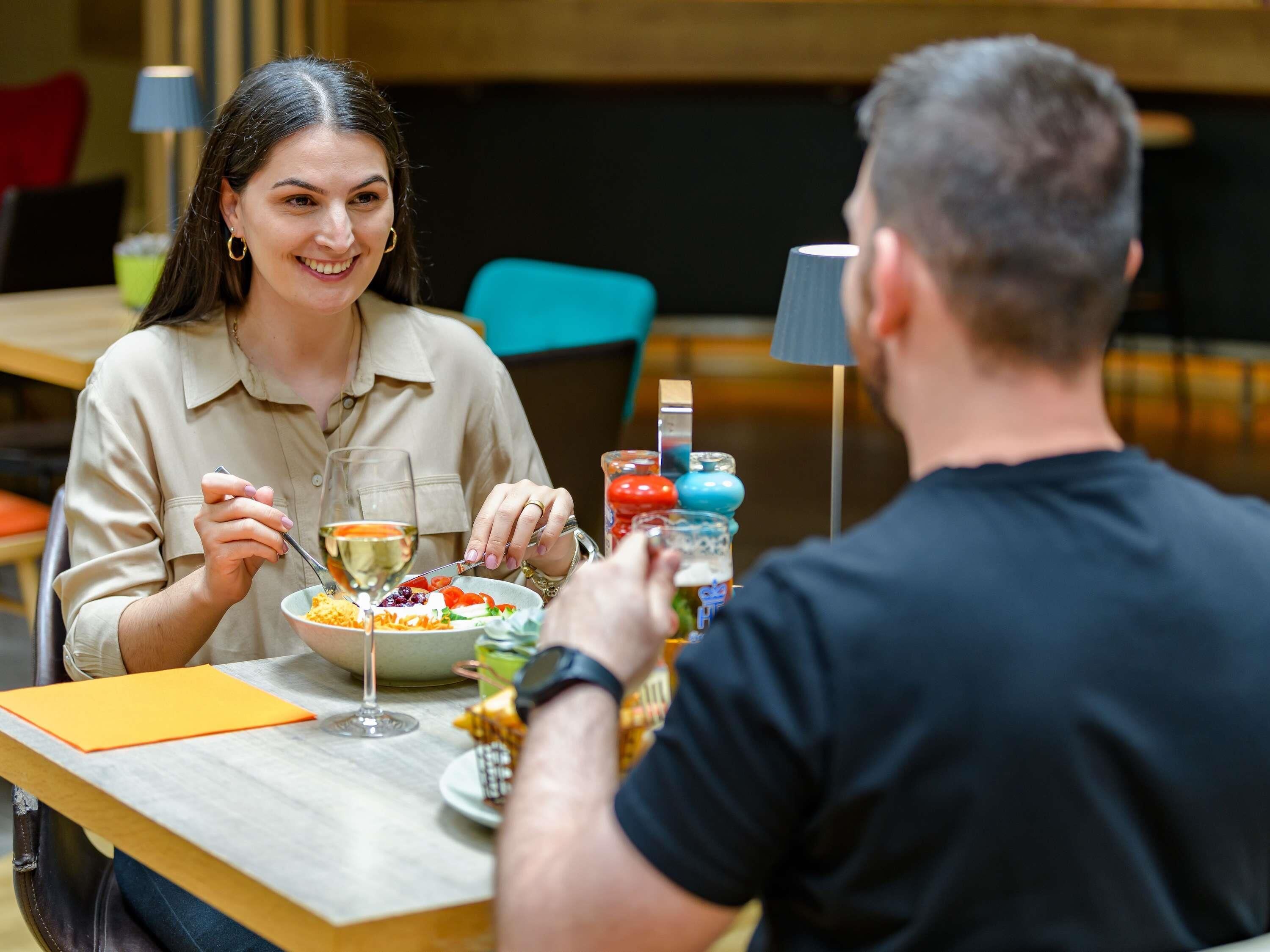 A dining table with a plate of food, a glass of wine, and a person eating.