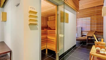 A modern spa room with wooden slats on the ceiling, a glass door leading to a sauna area, and a seating area with a table and chairs.