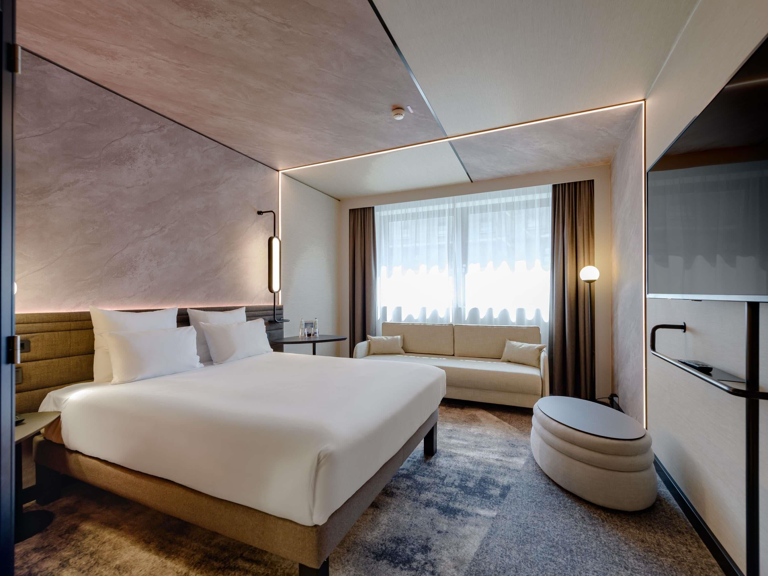 Une chambre d’hôtel moderne équipée d’un grand lit, d’un canapé, d’une petite table, d’une télévision et d’une salle de bain.