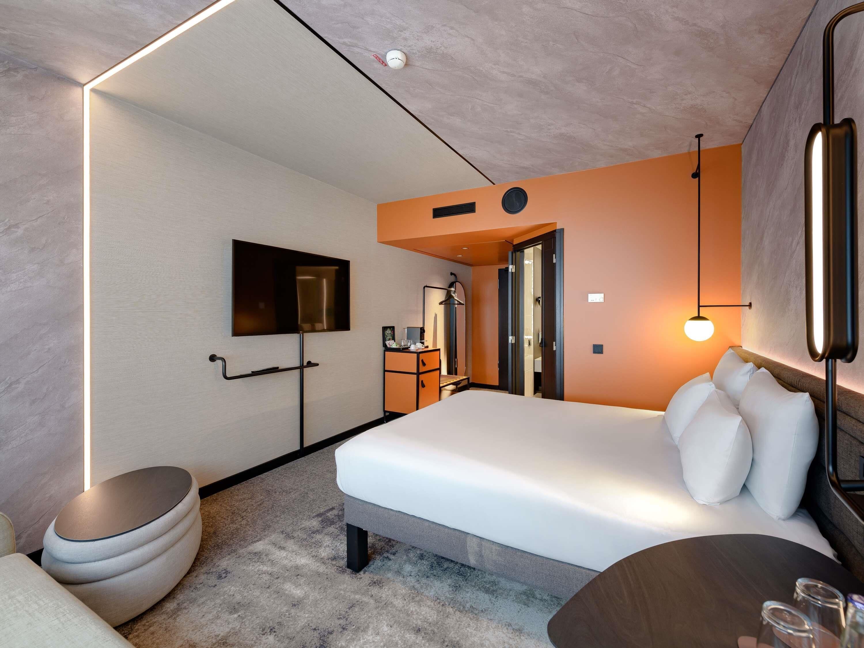 Habitación de hotel moderna con una cama grande, un televisor de pantalla plana, un escritorio con una silla y un pequeño rincón de estar.