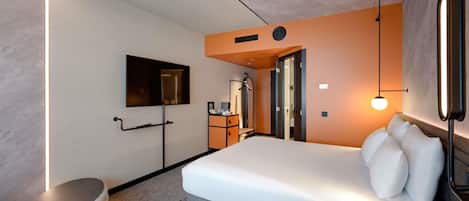 Habitación de hotel moderna con una cama grande, un televisor de pantalla plana, un escritorio con una silla y un pequeño rincón de estar.