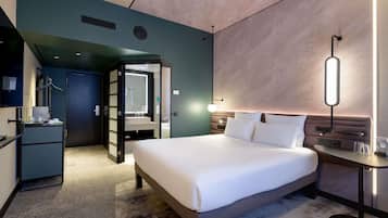 A modern hotel room with a large bed, bedside table, and a mirror.
