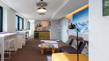 Ein modernes Hotelzimmer mit Küchenzeile, einer Sitzecke inklusive Sofa und Couchtisch sowie einem großen Fenster für natürliches Licht.