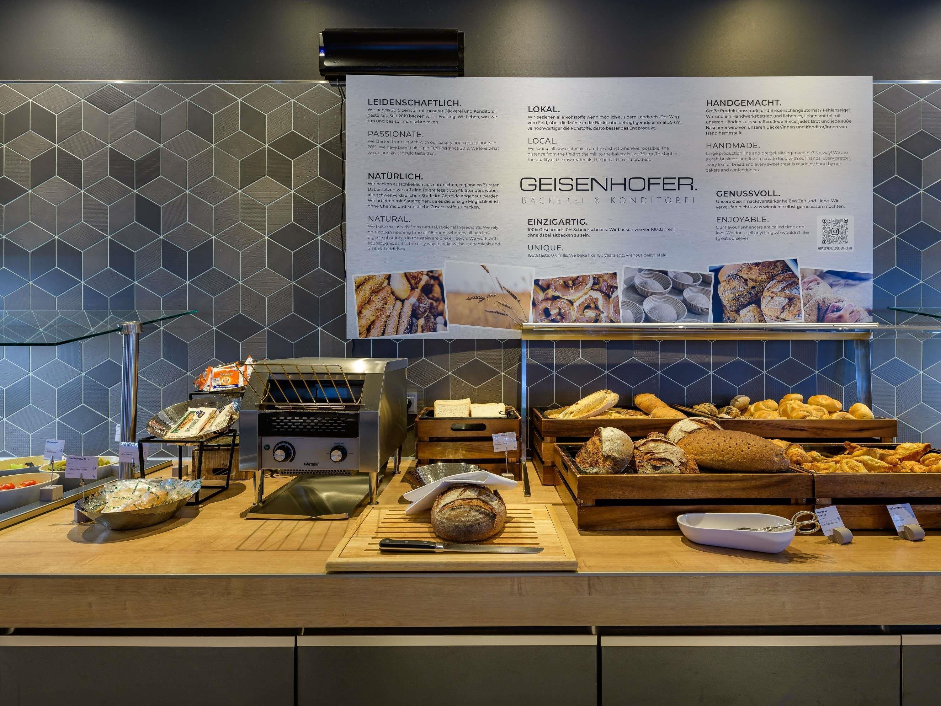 Vitrine de uma padaria com diversos pães e doces, um cortador de pão e uma placa com informações sobre as qualidades da padaria.