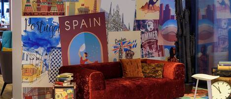 A travel-themed room with a red velvet sofa, a small table, and a clock. The walls are decorated with various travel posters and a map.