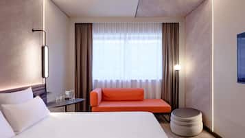 Una habitación de hotel con cama, sofá, mesita, lámpara y ventana con cortinas.