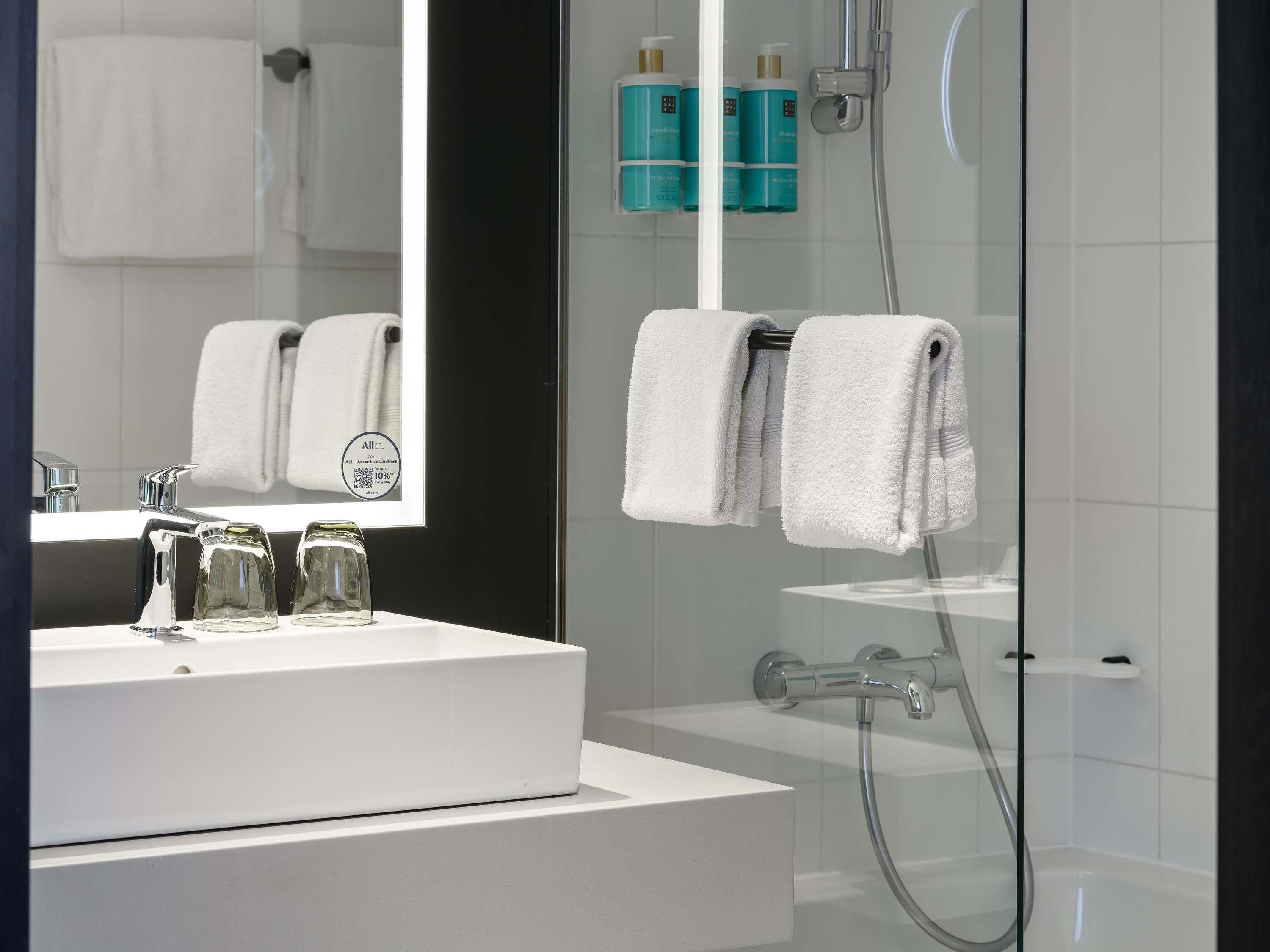 Ein modernes Badezimmer mit einem weißen Waschbecken, einem großen Spiegel und einer Duschkabine.