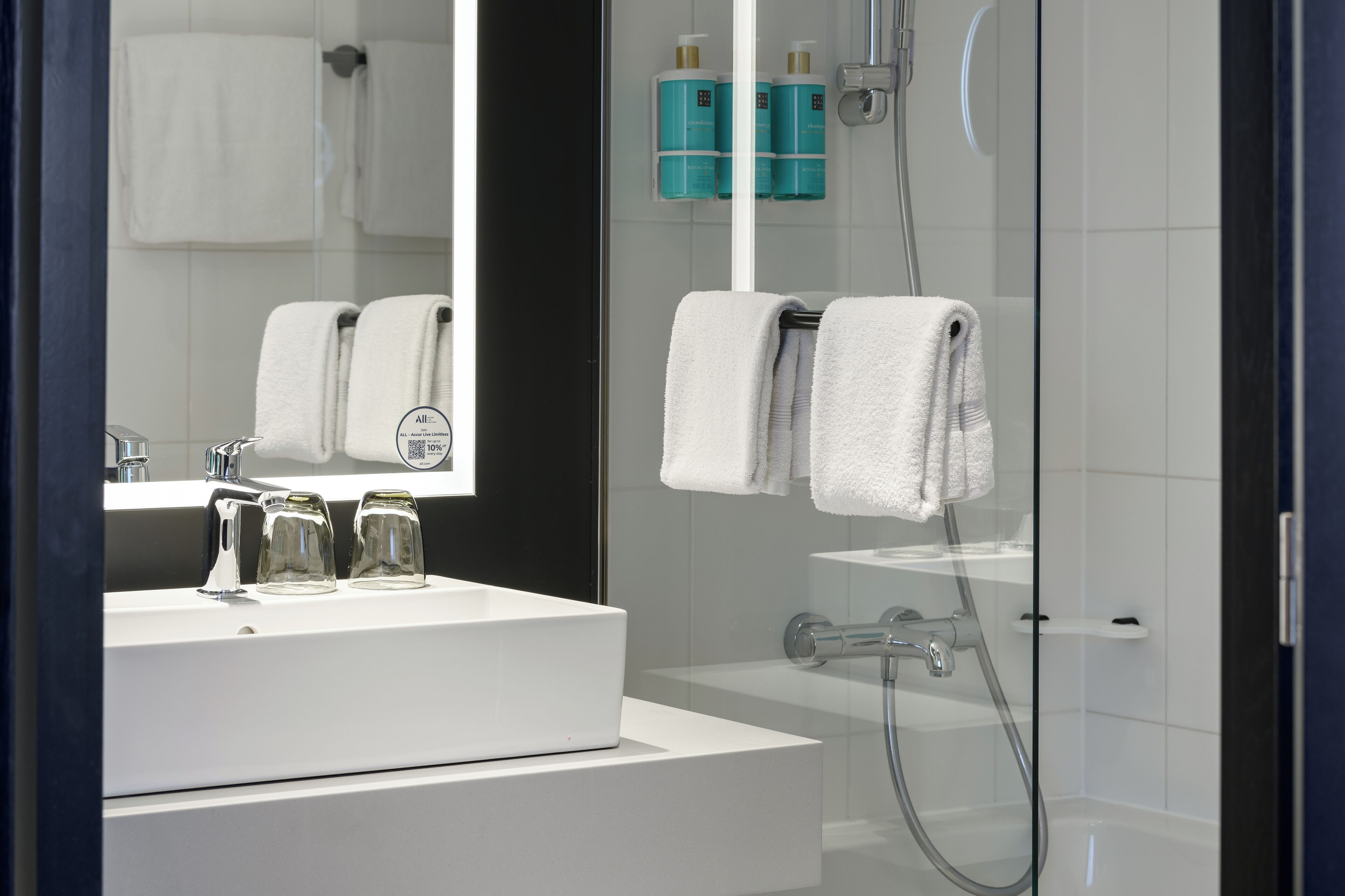 A modern bathroom with a white sink, a large mirror, and a glass shower enclosure.
