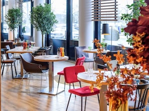 L’intérieur d’un restaurant moderne, avec des tables rondes, des chaises rouges et marron, et des plantes en pot.