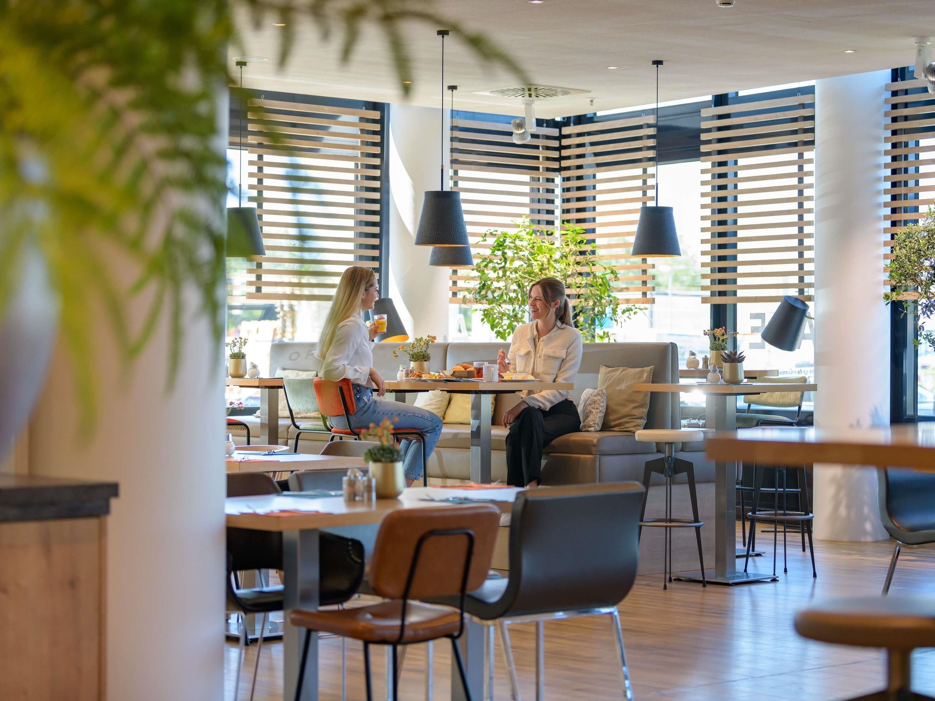 A modern cafe interior with wooden slats, pendant lighting, and potted plants.