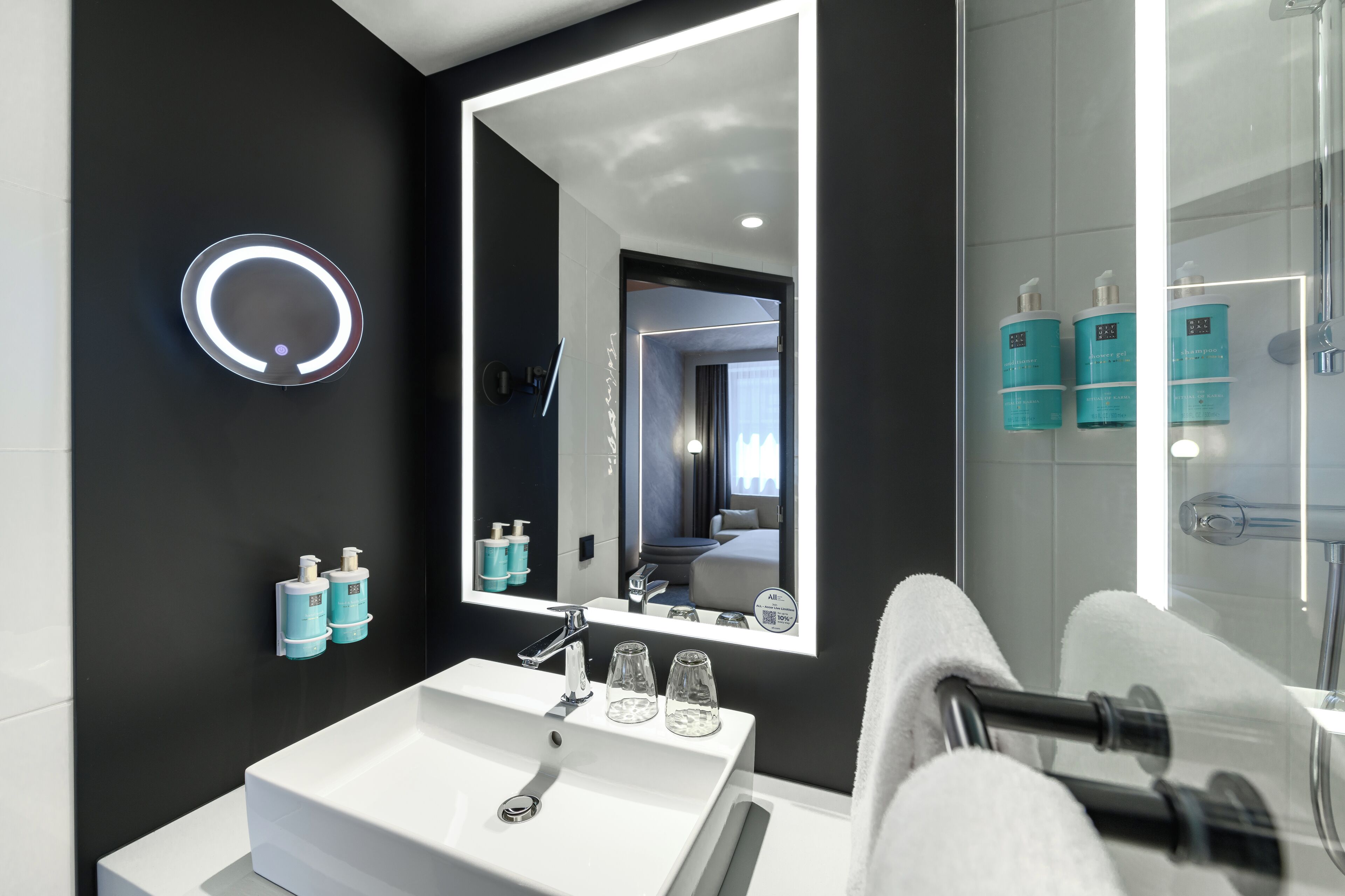Un baño moderno con un espejo grande, un lavabo blanco y dos botellas de champú.