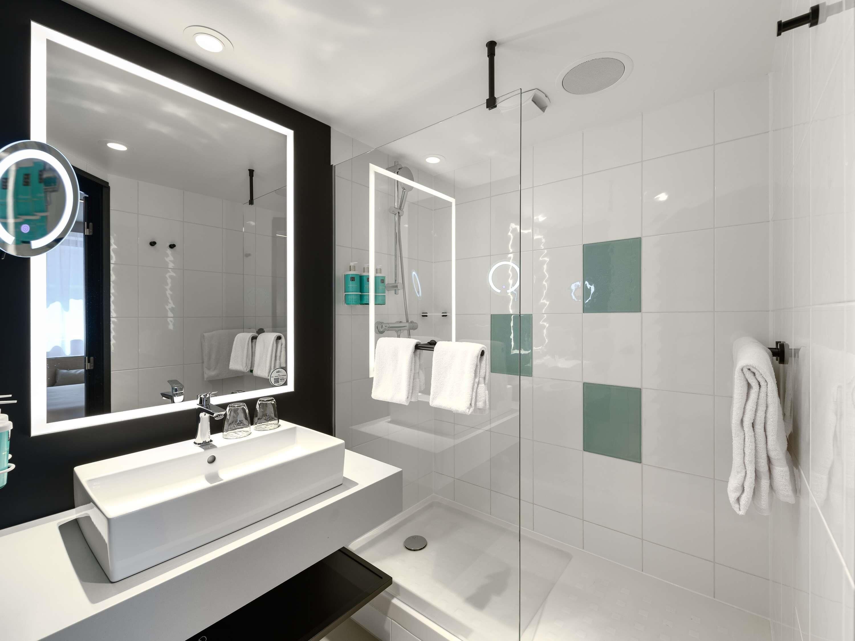 Een moderne badkamer met een grote spiegel, een witte wastafel en een douchecabine met glazen wanden.