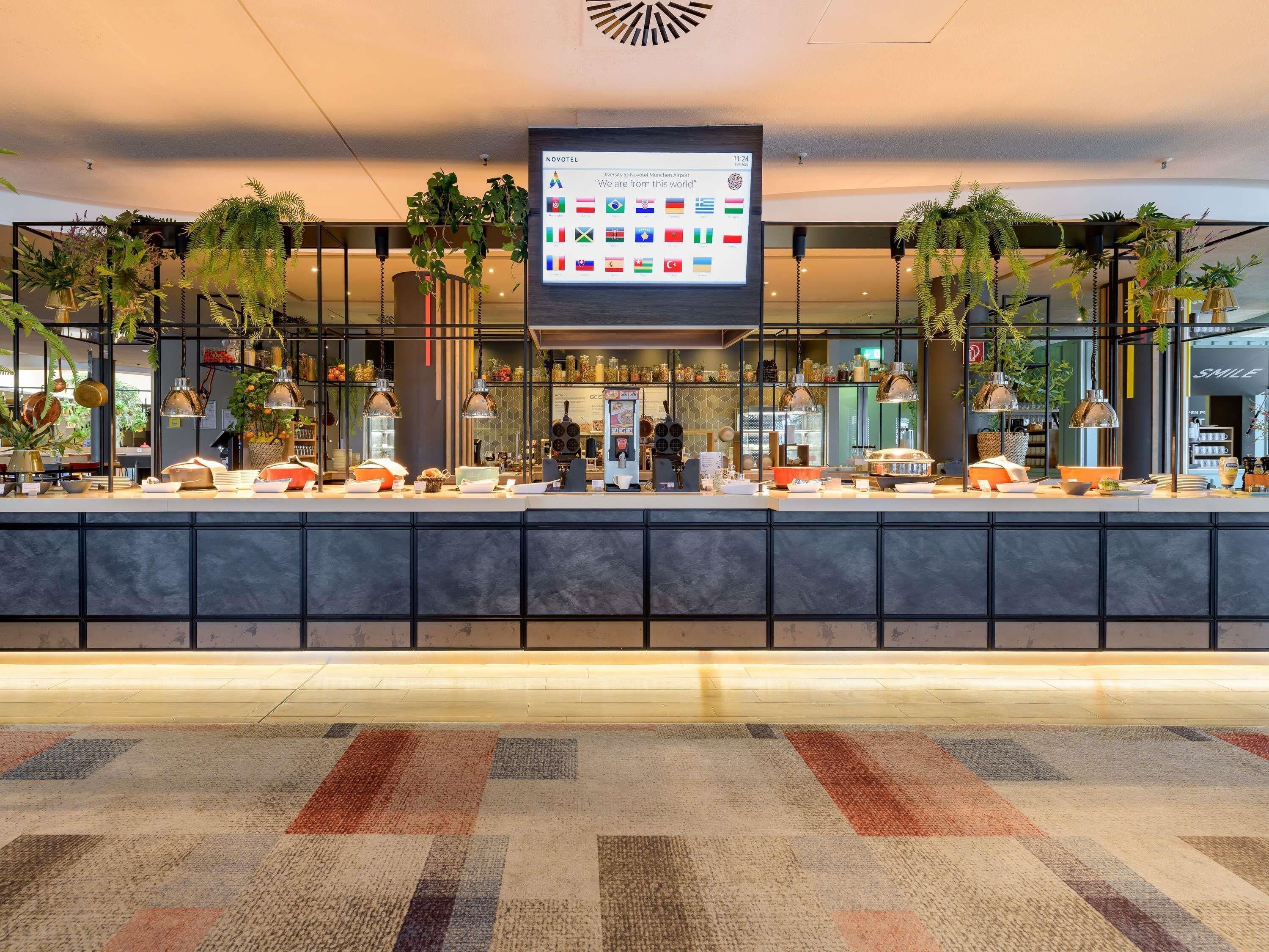Eine moderne Hotelhalle mit Empfangstresen, digitalem Bildschirm und Zimmerpflanzen.