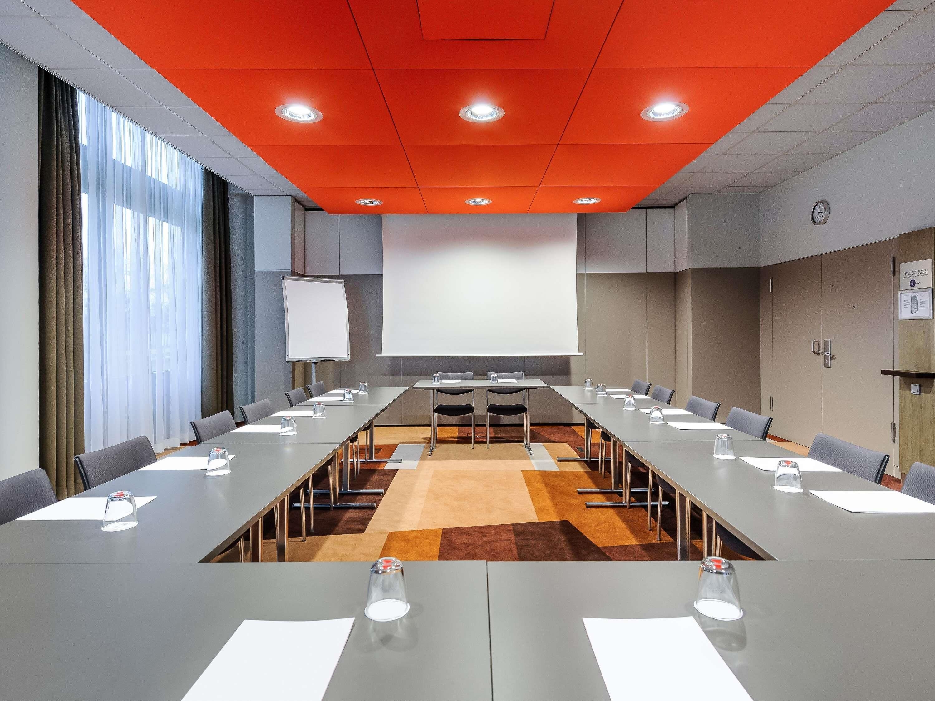 Une salle de conférence avec une longue table, des chaises, un écran de projection et une horloge au mur.