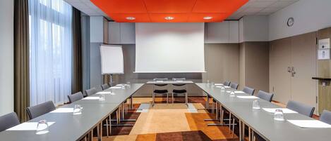 Une salle de conférence avec une longue table, des chaises, un écran de projection et une horloge au mur.