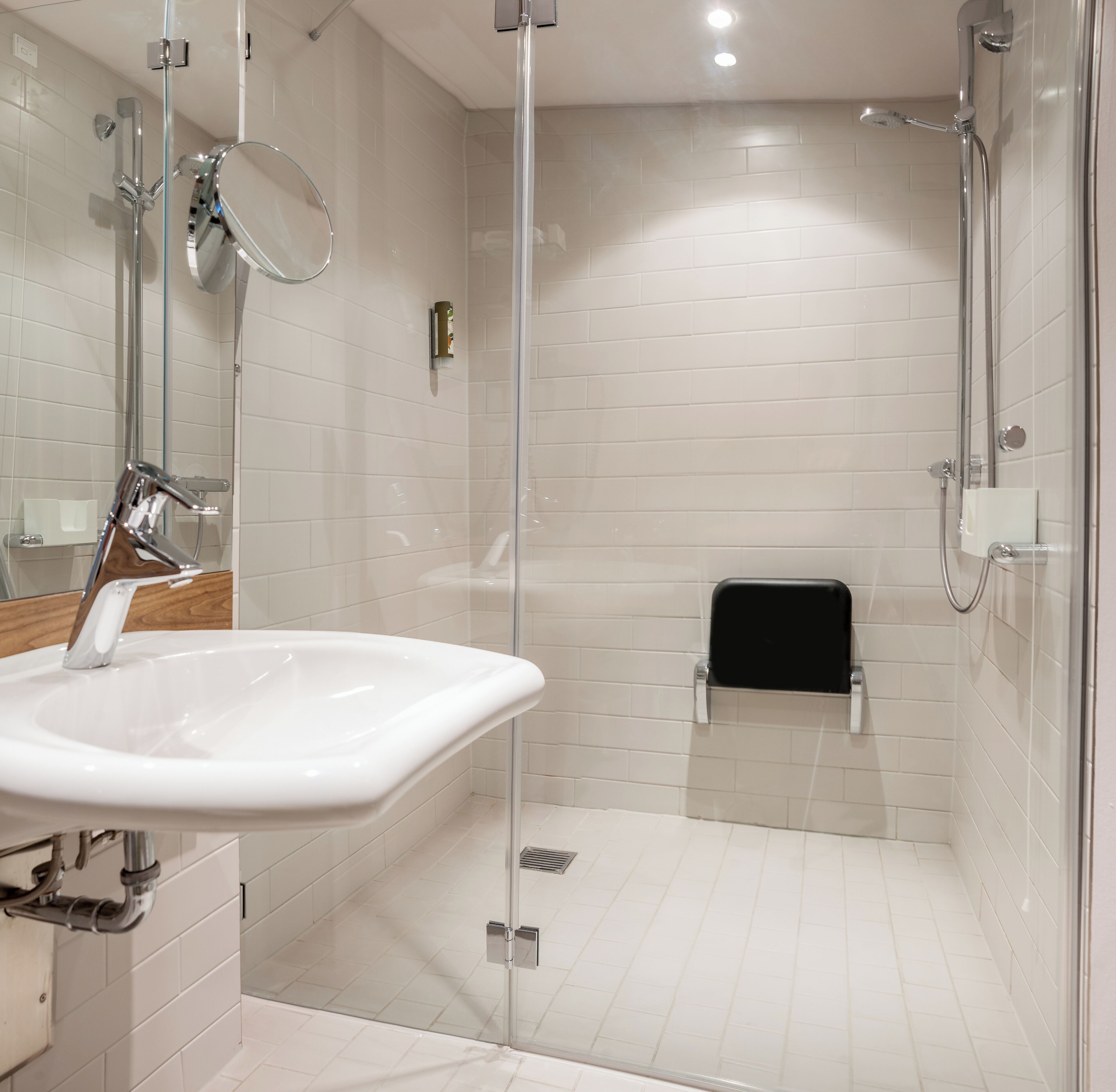 Een moderne badkamer met een douchecabine van glas, een witte wastafel en een spiegel.