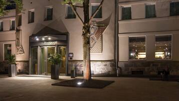 A hotel entrance with a glass door, a tree in the foreground, and a stone wall with a checkered pattern.