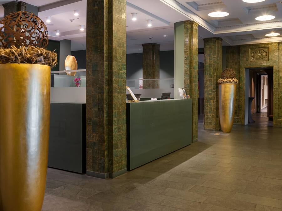 A reception area with a green reception desk, large decorative vases, and a modern interior design with stone columns and recessed lighting.