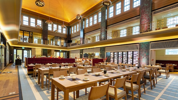 Un vaste espace dédié à la salle à manger, doté de nombreuses tables et chaises, de hauts plafonds et de grandes fenêtres laissant entrer la lumière naturelle.