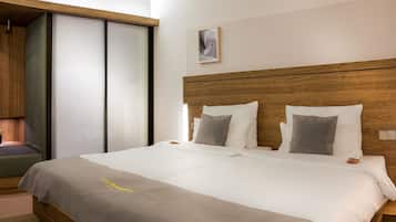 A hotel room with a wooden headboard, a bed with white and gray bedding, a bedside table, and a small window.