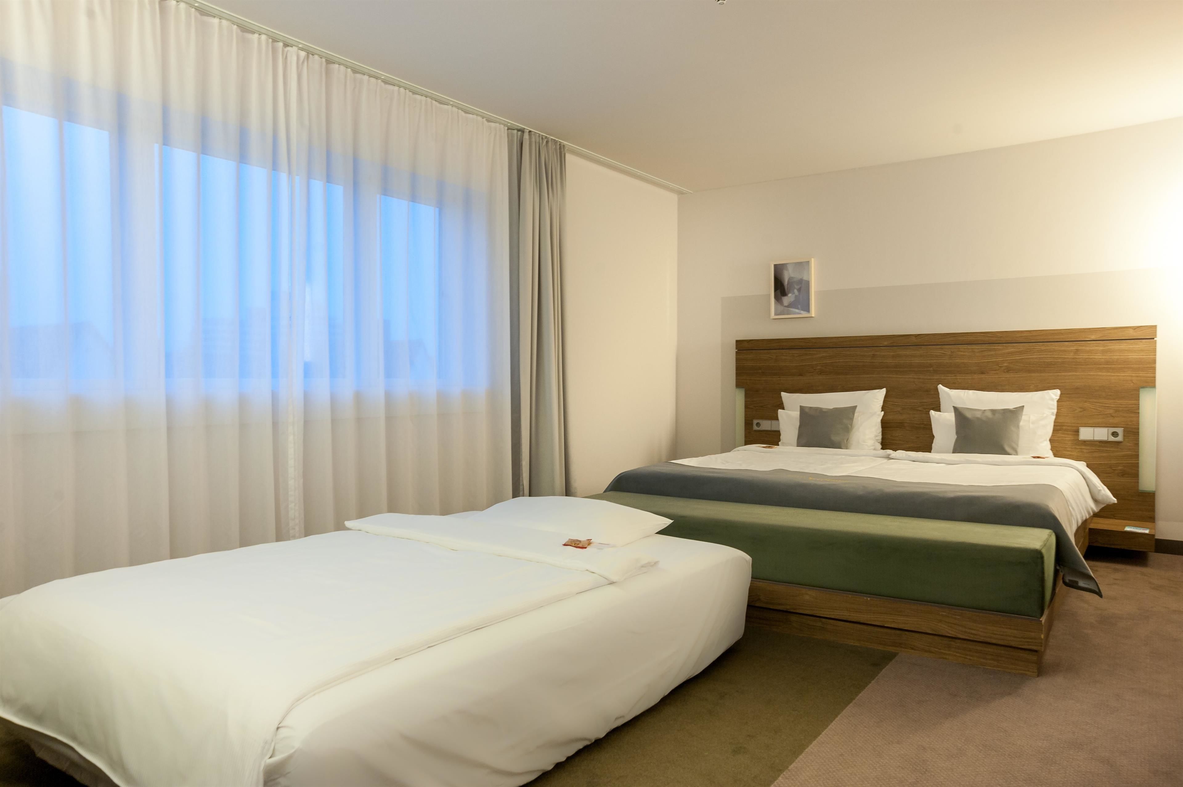 A hotel room with two beds, a wooden headboard, and a large window with sheer curtains.