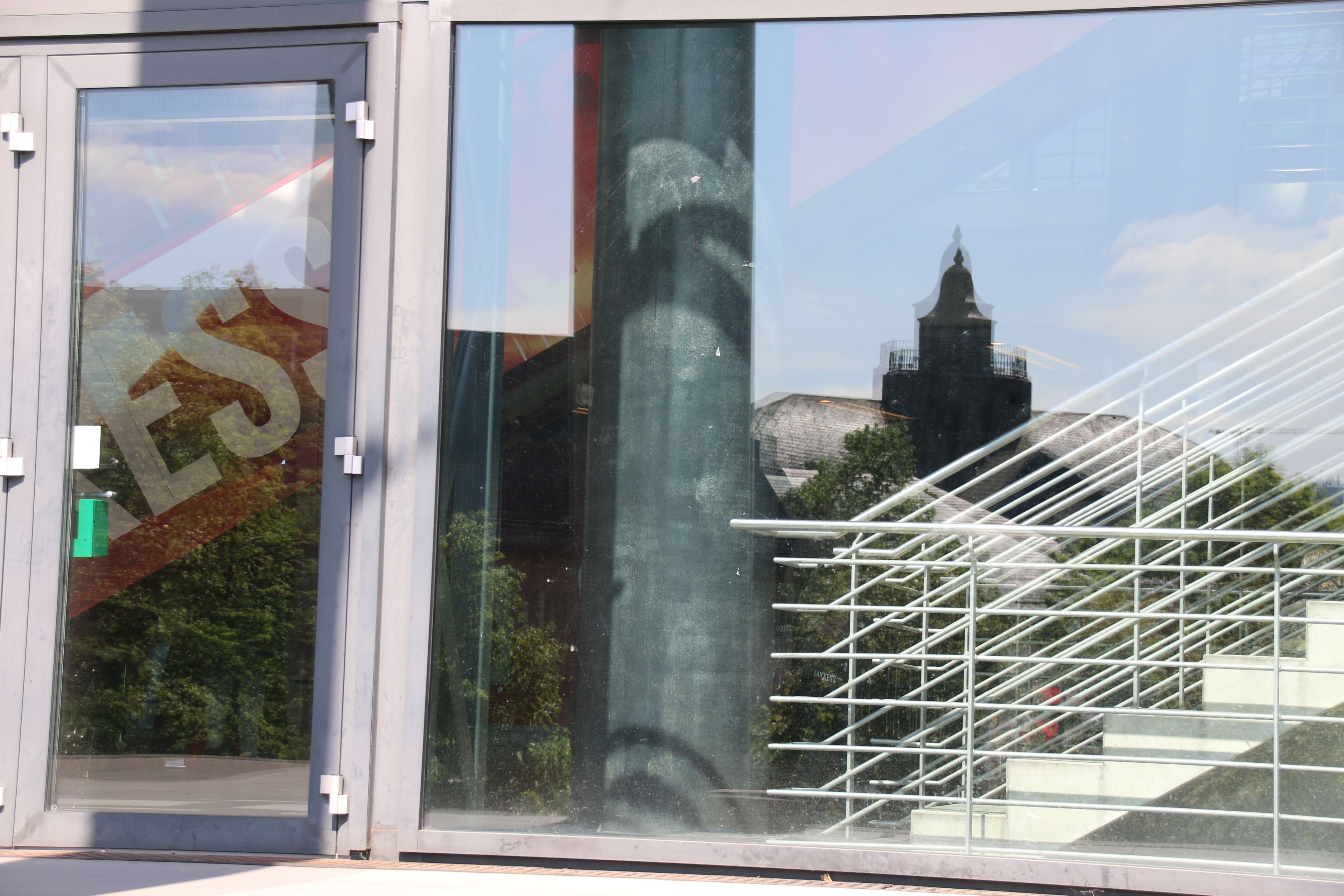 Ein moderner Gebäudeeingang mit Glastür, einer Metalltreppe und einem Spiegelbild eines Turms.