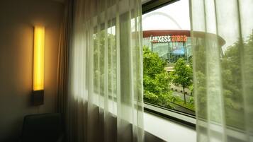 Ein Hotelzimmer mit Blick auf die LANXESS Arena durch transparente Vorhänge.