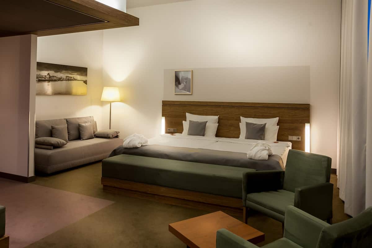Quarto de hotel com cama, sofá, poltrona, mesa e abajur.