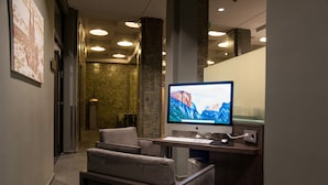 Un espace d’accueil d’hôtel comprenant un bureau avec un ordinateur, une chaise et un grand écran affichant un paysage de montagne.
