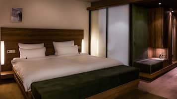 A modern hotel room with a large bed, wooden headboard, and a built-in bench with a side table.